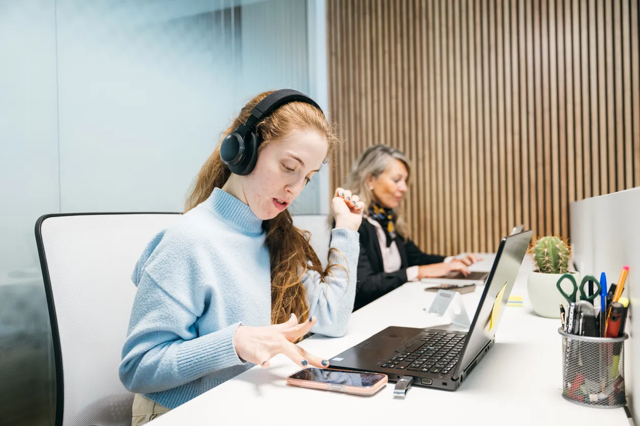 A woman wearing headphones works on a laptop in an office