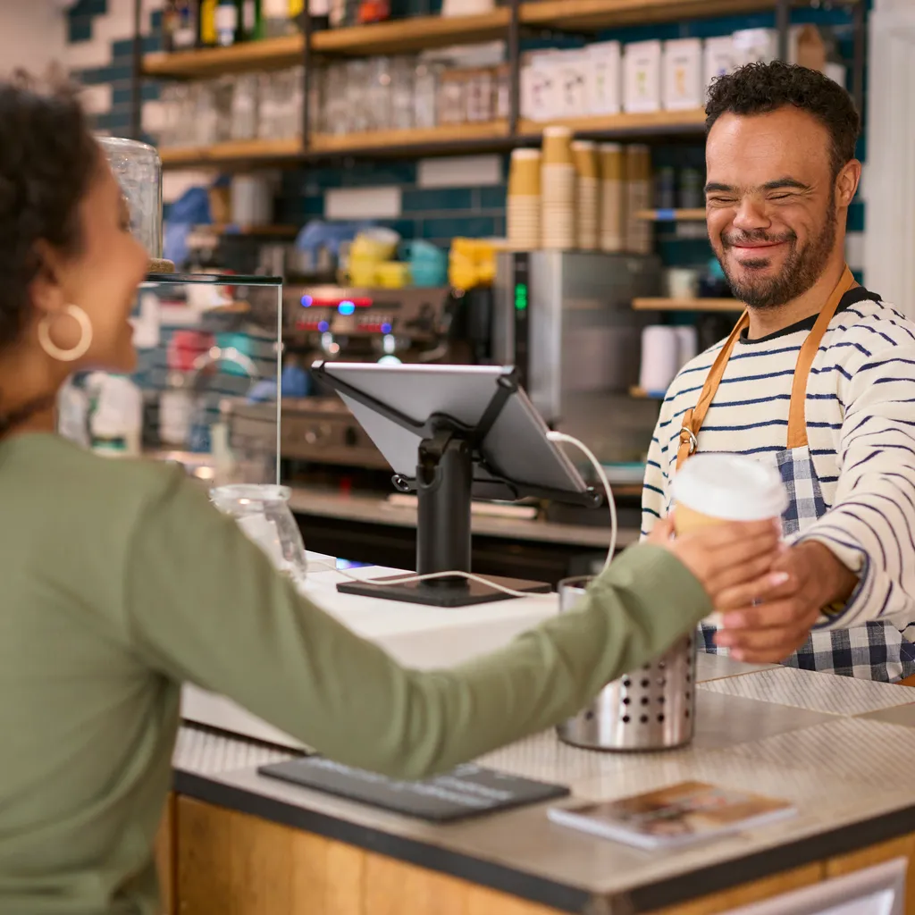 Person with an intellectual disability serving a customer coffee in a coffee shop